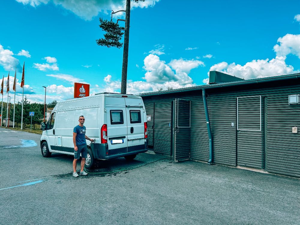 Ragazzo mentre rifornisce di acqua il camper durante una sosta rifornimento in Finlandia on the road