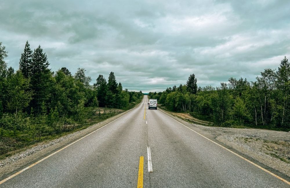 Furgone mentre percorre una strada in Finlandia che taglia una foresta di pini e betulle