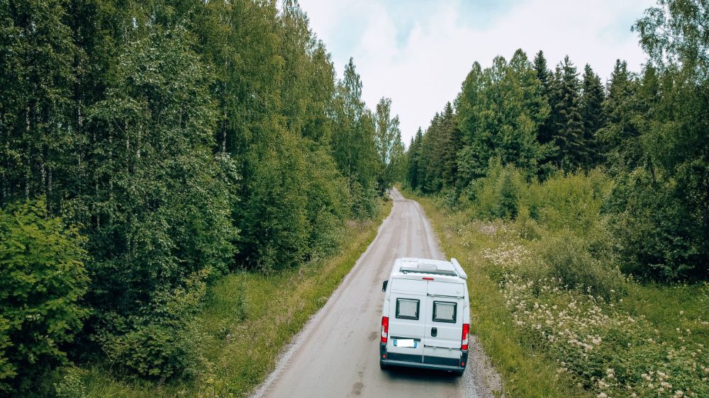 Finlandia on the road: camper attraversa una strada sterrata in mezzo al bosco